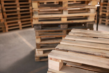 Many empty wooden pallets stacked in warehouse, closeup. Space for text