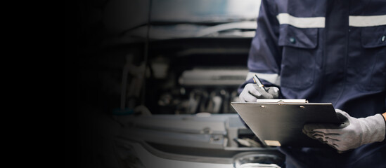 Car service, repair, maintenance concept,auto mechanic man or Smith writing to the clipboard at workshop, technician doing the checklist for repair machine a car in the garage,banner.