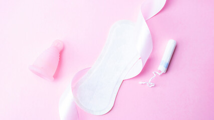 Menstrual pads, menstruation cup and tampon for woman hygiene on pink background. Menstruation feminine period. Flat lay banner, copy space for text. Gynecological care.