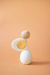 Boiled egg stacked in order, all components of the eggs shown on light orange background. Side view, interesting concept.