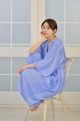 白い窓を背景に椅子に座りくつろぐドレスを着た若い女性	
