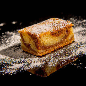 Besquit, cake on a black background, sprinkled with powdered sugar, dark and light layer of beckett on a black background, copy space