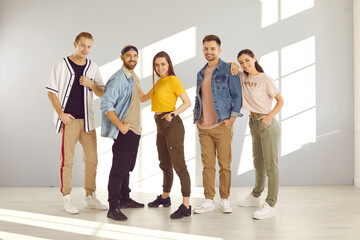 Group portrait of happy confident young people wearing modern beautiful casual clothes. Models in comfortable pants, sneakers, T shirts, denim jackets and bandana headband scarves posing in studio