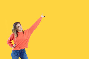 Beautiful young woman standing isolated on yellow, looking up, smiling and pointing index finger to...