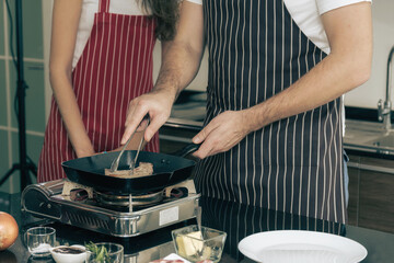 Close-up shot of couple cooking a steak on the stovetop.