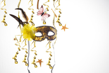 Gold and black carnival mask with streamers, butterfly, feathers and yellow flower on white...