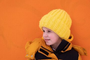 Portrait of a teenage girl. Child in winter clothes of bright yellow shades. Bright orange background. Stylish photo, bright colors. Knitted hat in bright yellow