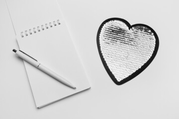 Top view of open spiral blank notebook with pen and heart on sequins.