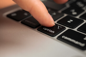 Hand pressing option key on modern laptop keyboard. Option sign and symbol close-up