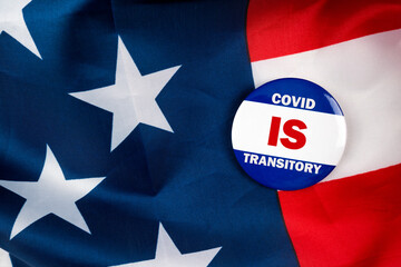 covid is transitory text quote on election button laying on the star spangled banner. united states of america concept.