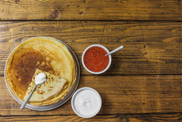 Pancakes with sour cream and caviar on a wooden background. Maslenitsa. Top view