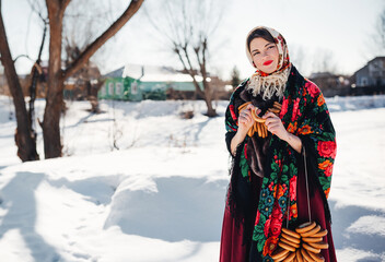 Outdoors lifestyle portrait of pretty young woman in a traditional Russian headscarf with bagels on winter background. Shrovetide. Wearing a Russian folk clothes. Russian style. Maslenitsa festival.