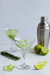 martini with lime and rosemary. Cucumber water with lime. martini glass of lemonade and shaker with slices of lime and cucumber on the white table. cold alcohol drinks with copy space.