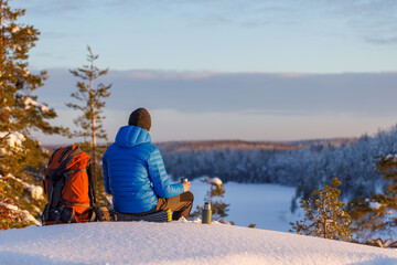 Relaxed man drinking delicious hot tea in winter forest.
