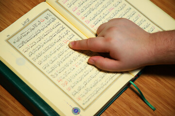 Naklejka premium reading quran and pointing to word of allah with finger. photo inculuding arabic letter from quran verses