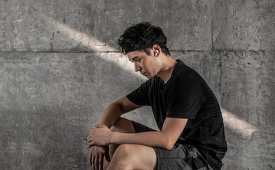sports man wearing bluetooth earphone is resting near the gray wall 