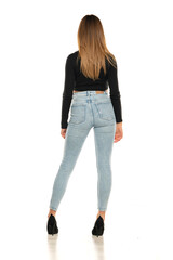Rear view of a young woman standing in studio in black short blouse and blue jeans on a white background