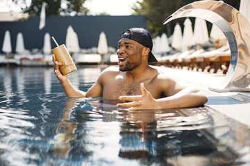 Portrait of a black american man standing in a swimming pool with cocktails