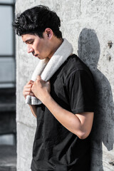 sports male resting against the wall with towel on his shoulder