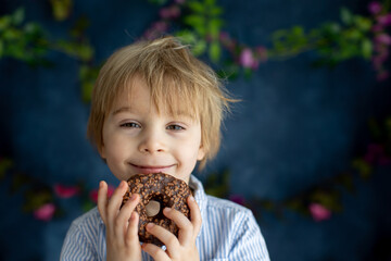 Naklejka premium Cute little blond child, preschool boy, eating pink donut in the shape of heart, made for Valentine