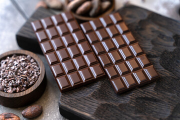 Stack of chocolate bars with cocoa beans. Flat lay composition with delicious chocolate on black background. Space for text