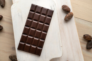 Dark bitter chocolate bar with cocoa beans on a wooden white background, top view. delicious chocolate. Space for text
