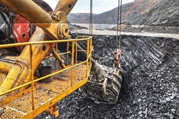 A mining excavator bucket digs iron ore in a quarry. View from the cab of the excavator driver