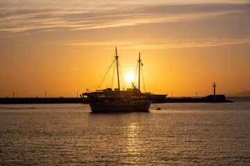 Sunset over Mykonos island, Cyclades, Greece. Moored ship at port, beacon orange sky sparkle sea.