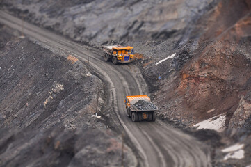 Extraction of iron ore. A mining dump truck transports iron ore along a side carrea. Special equipment works in a quarry