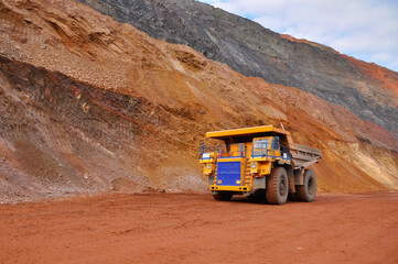Extraction of iron ore. A mining dump truck transports iron ore along a side carrea. Special equipment works in a quarry