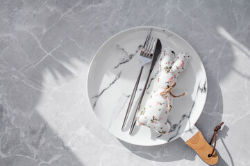 Banner. Table setting. A fashionable marble plate with a rabbit on a napkin, Easter eggs and feathers on a gray background. Top view. Happy Easter holiday concept for cafes and restaurants.