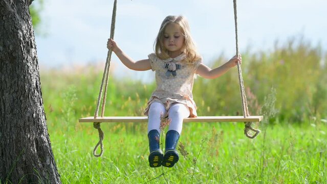 Happy cute girl swinging on a swing in the park. Little cheerful girl laughs. Concept of happy family and childhood.