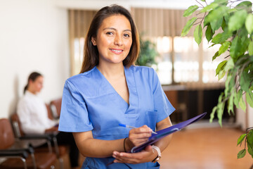 Young woman healthcare worker in blue overall posing in medical office