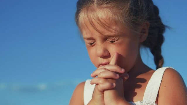 girl kid pray against a blue sky. child close-up concept faith religion and happy family. kid daughter jew crossed arms praying to god. kid pray worship and gratitude and a catholic happy childhood
