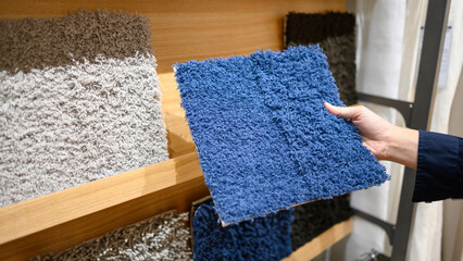 Male hand choosing color and texture of synthetic carpet or rug samples in furniture store showroom. Interior design and home decoration concept.