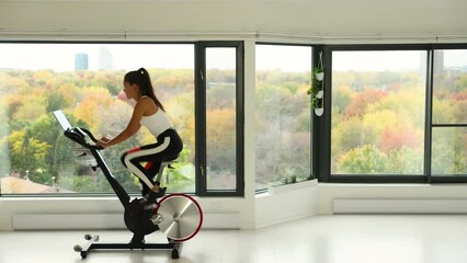 Exercise bike with wheels spinning. Woman exercising at home living room on indoor bicycle doing workout. Woman training on stationary bike watching online video class using training fitness app - Powered by Adobe