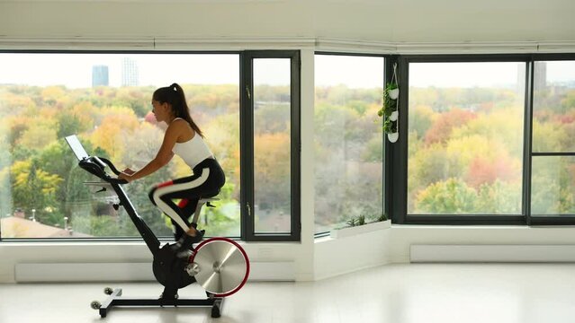 Exercise bike with wheels spinning. Woman exercising at home living room on indoor bicycle doing workout. Woman training on stationary bike watching online video class using training fitness app