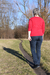 Neue Wege gehen. Eine Frau mit rotem Pullover wandert in einem Park auf einem Trampelpfad im Herbst...