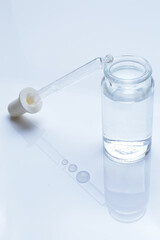 glass transparent jar and a cosmetic pipette with liquid droplets on a white background.