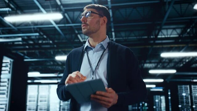 Male IT Specialist Walks Between Row of Operational Server Racks in Data Center. Engineer Uses Tablet Computer for Maintenance and Diagnostics in Cyber Security and Data Protection Facility.