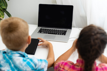 Boy and girl, brother and sister study at home. A girl watches a video lesson or an online conference, a boy does exercises in a notebook from a textbook