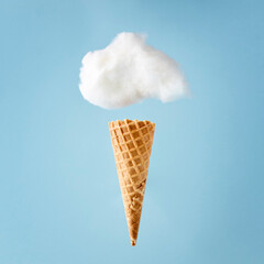 White cloud made of fluffy cotton over an ice cream cone against pastel blue background.