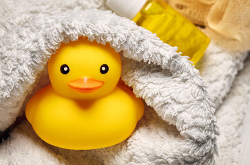 Yellow rubber duck toy wrapped in a white towel in the bathroom. Baby or child bath time