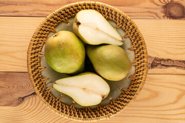Two halves of an organic sweet pear and two whole pears in a ceramic dish on a wooden table, macro,...