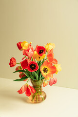 Fototapeta premium Big flowers bouquet of multicolored tulips in vintage glass vase on beige color background with copy space. Business card. Invitation postcard. Place for greeting text. International holiday. Banner.