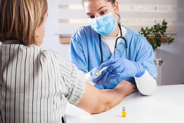 Young female doctor vaccinating elderly patient in UK GP's office