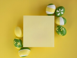 Frame of painted Easter eggs with yellow and green stripes and flowers at the corners of a yellow square with space for text. Easter card concept.