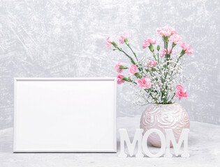 Mock up white empty frame, round vase of carnation and gypsophila flowers, white wooden MOM letters.