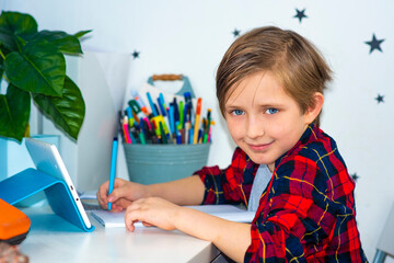 Distance learning online education. schoolboy studying at home with digital tablet in hand and doing school homework. 