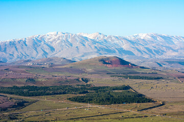 Mount Hermon in Israel in the winter with the Golan Heights beneath with roads and green fields.